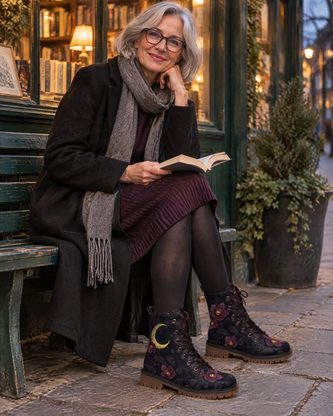 A smiling silver-haired woman on a bench outside a bookshop, wearing Vespertine moon-print boots